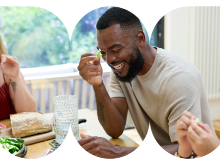 Person enjoying a meal with others, holding a celery stick at a dining table with salad and bread nearby.