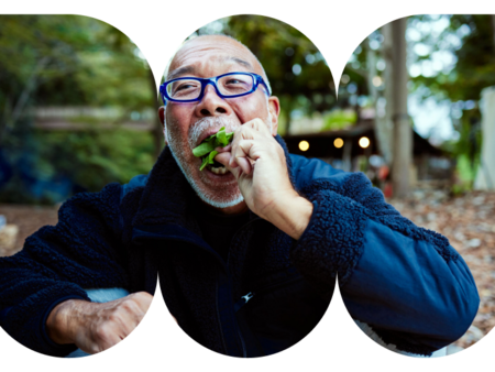 Person wearing glasses eating leafy greens while seated outdoors in a wooded setting.